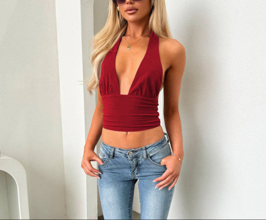 Woman wearing a red halter top and blue jeans with sunglasses indoors.