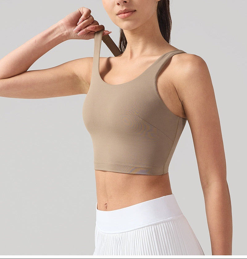 Woman wearing a beige sports bra and white pants against a gray background