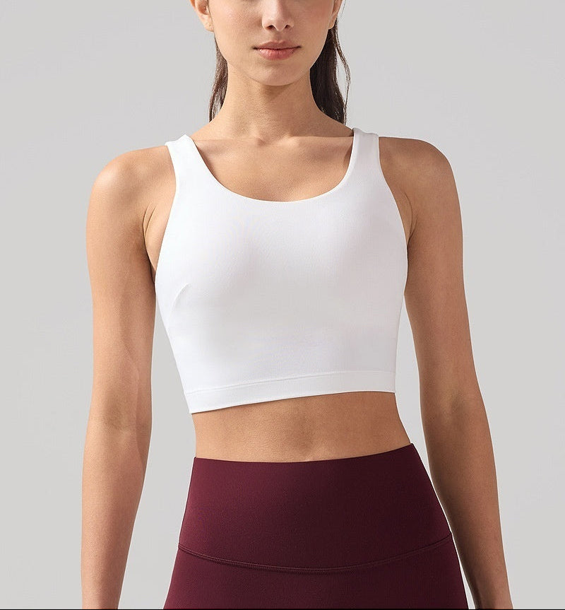 Woman wearing a white tank top and maroon leggings on a gray background